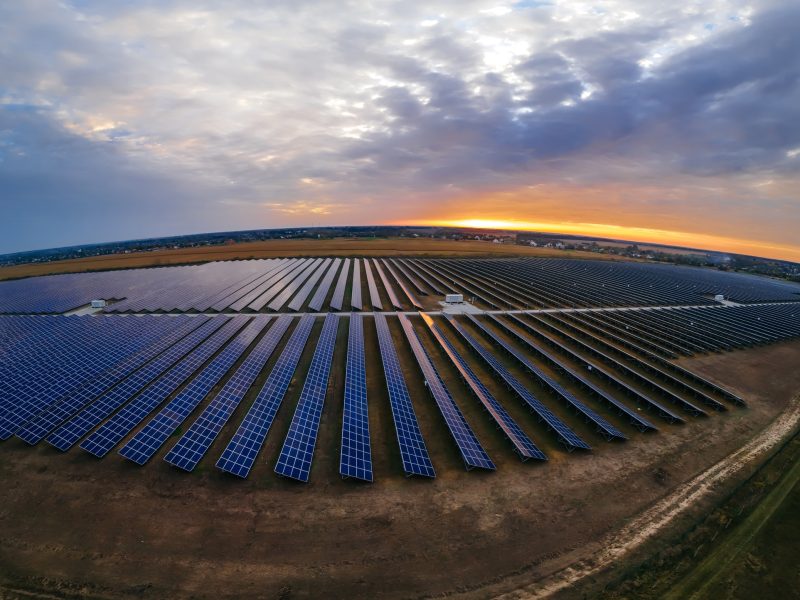 Aerial drone view into large solar panels at a solar farm at bright sunset. Solar cell power plants.